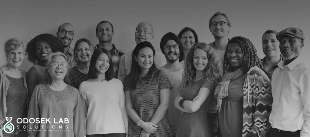 A diverse group of people of various ages and ethnicities smiling and posing together for a group photo. The background is a gradient from dark to light gray. The logo reads "ODOSEK LAB SOLUTIONS" with a tagline "Your Lab Partner Anywhere You Are.